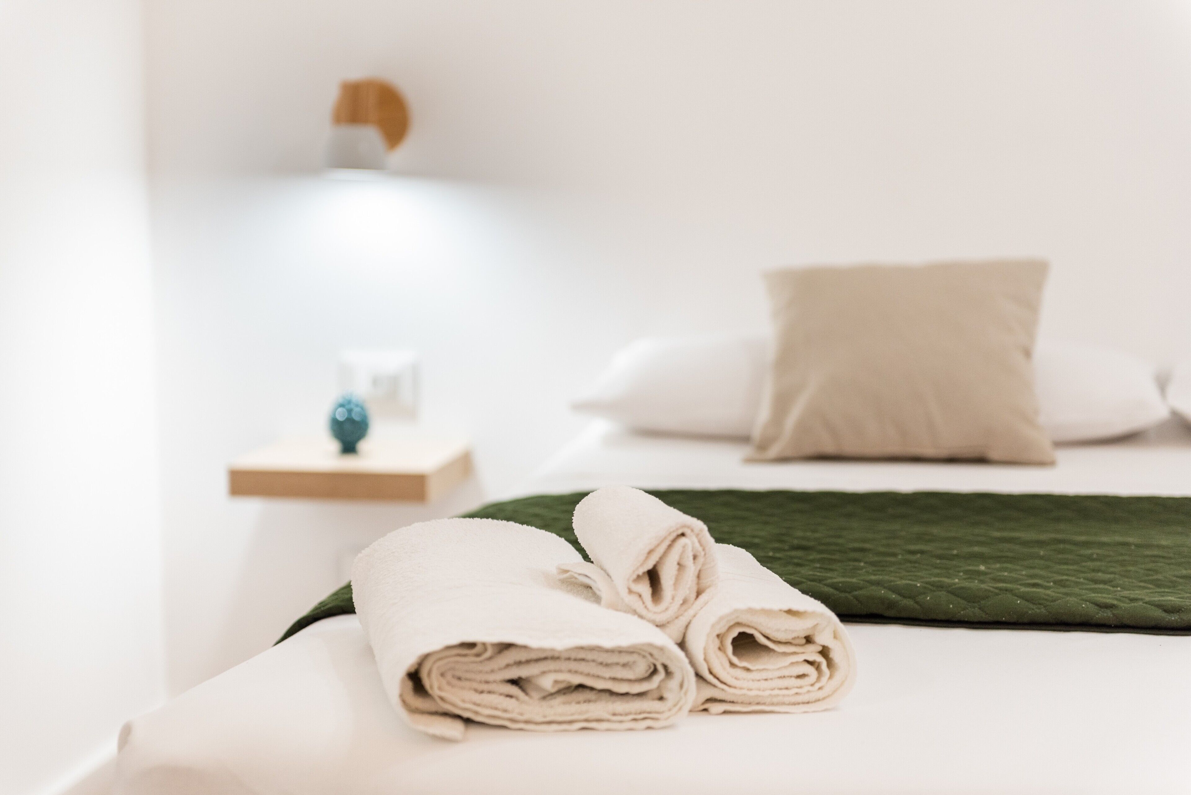A neatly made bed with rolled towels, a green blanket, and a white pillow.