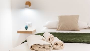 A neatly made bed with rolled towels, a green blanket, and a white pillow.