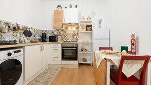 A compact kitchen with a washing machine, oven, microwave, and a dining area with a table and chairs. - 'Il Cortile Holiday House - Dimora Maiolica' Apartment with Wi-Fi and Air Conditioning (Caccamo)