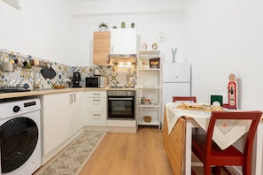 Ett kompakt kök med tvättmaskin, ugn, mikrovågsugn och en matplats med bord och stolar.