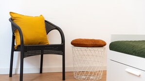 A black wicker chair with a yellow cushion, a white wire basket with a brown cushion, and a white dresser with a green bedspread. - 'Il Cortile Holiday House - Dimora Maiolica' Apartment with Wi-Fi and Air Conditioning (Caccamo)