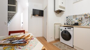 A compact kitchen with a washing machine, a TV mounted on the wall, and a patterned backsplash. - 'Il Cortile Holiday House - Dimora Maiolica' Apartment with Wi-Fi and Air Conditioning (Caccamo)