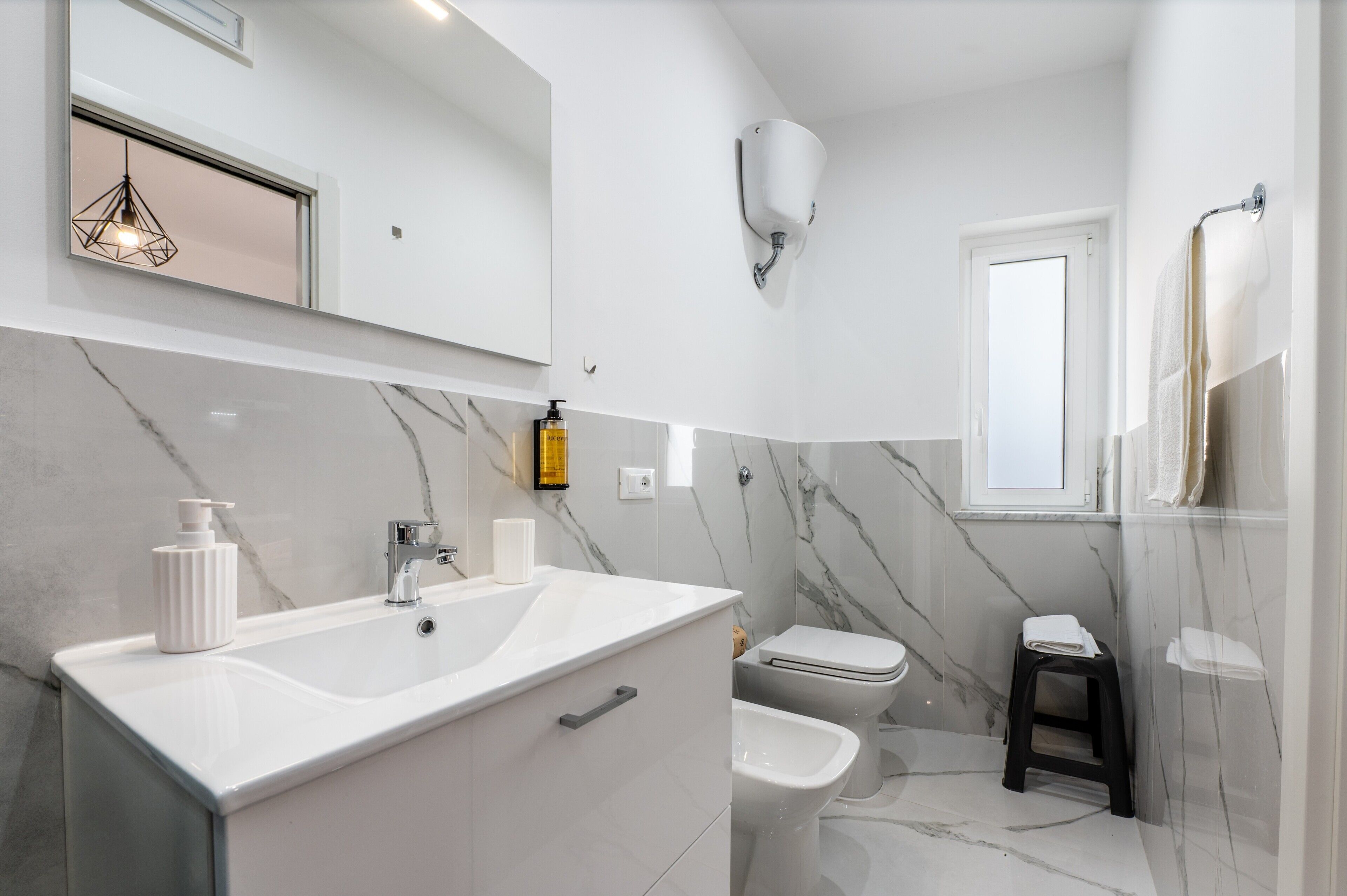 A modern bathroom with a white vanity, a toilet, a bidet, a towel rack, and a mirror.