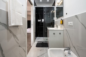 Casa de banho moderna com cabine de duche em vidro, lavatório branco e chão em mosaico de mármore.