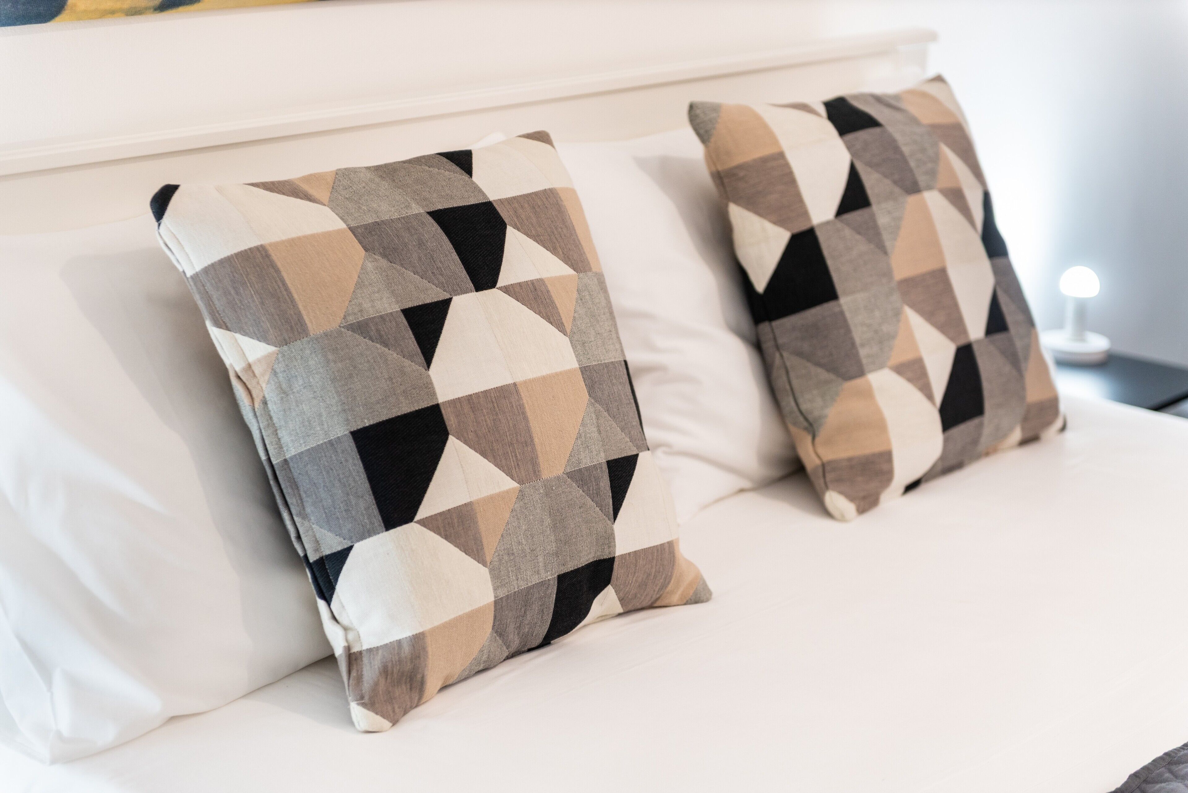 Una cama con dos almohadones estampados y un cabecero blanco.