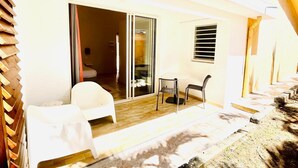 A room with a bed, a chair, a table, and a sliding glass door leading to an outdoor area with a table and chairs. - Studio Colibri - Terrace 2 pers, 3mn from Anse Mitan beach (Les Trois-Îlets)