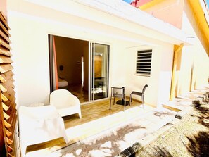 Una habitación con cama, una silla, una mesa y un ventanal corredero que da a un espacio al aire libre con mesa y sillas.