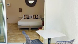 A room with a bed, a round mirror on the wall, a small table, and two chairs. - Studio Colibri - Terrace 2 pers, 3mn from Anse Mitan beach (Les Trois-Îlets)