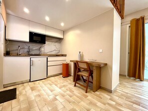 A compact kitchen with a microwave, sink, and small refrigerator. There's a wooden table with a chair and a waste bin. - Studio Colibri - Terrace 2 pers, 3mn from Anse Mitan beach (Les Trois-Îlets)