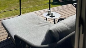 Un balcon avec une table et des chaises, une construction à toit de chaume et une vue sur un champ verdoyant et des montagnes.