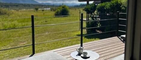 Un balcon avec une table et des chaises, une construction à toit de chaume et une vue sur un champ verdoyant et des montagnes.
