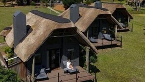 Une rangée de charmantes chaumières aux toits de chaume, dotées d’espaces extérieurs aménagés pour s’asseoir, se dressant dans un champ verdoyant sous un ciel dégagé.