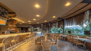 A restaurant with a bar area, wicker furniture, and a view of greenery.