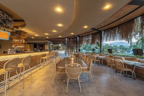 A restaurant with a bar area, wicker furniture, and a view of greenery. - Defne Beach Karya (Fethiye)