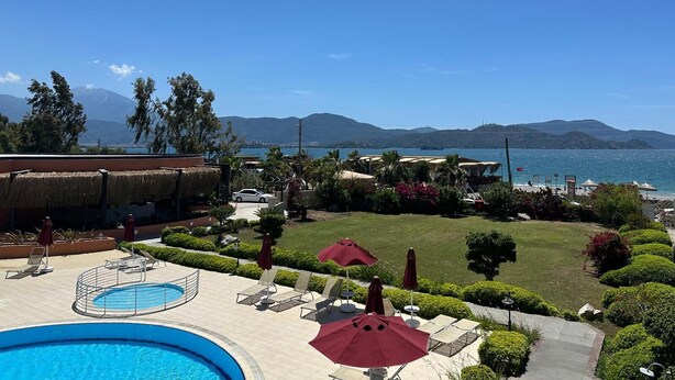 A pool area with lounge chairs and umbrellas, a view of the sea, and mountains in the background.