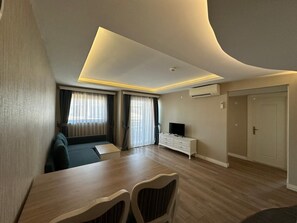 A modern living room with a dining area, a flat-screen TV, and an air conditioning unit.