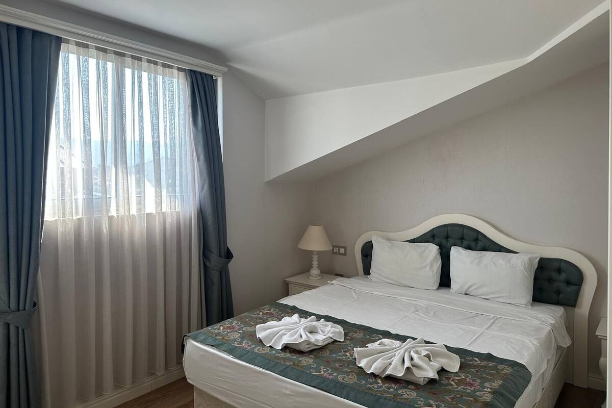 A hotel room with a bed, a nightstand, a lamp, and a window with curtains.