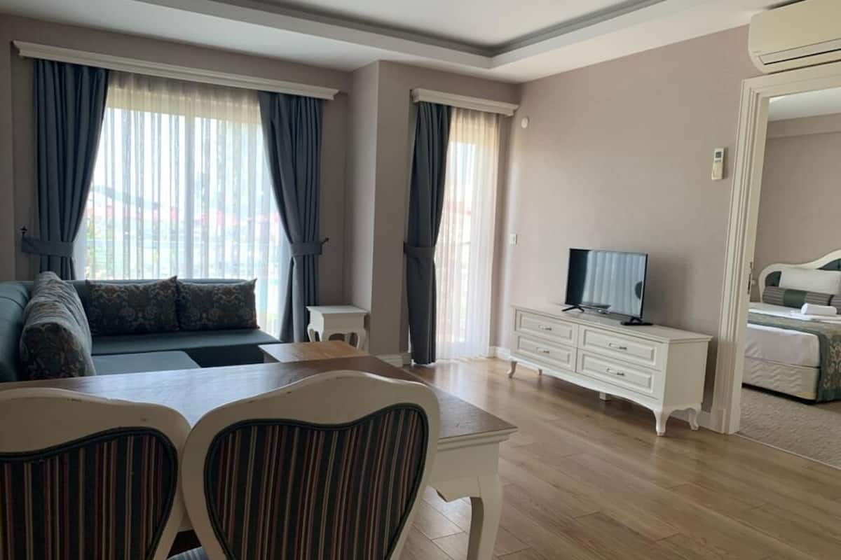 A hotel room with a sofa, a TV, a dining table with chairs, a white dresser, and a bed.