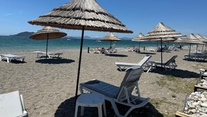 A beach with thatched umbrellas and white lounge chairs.