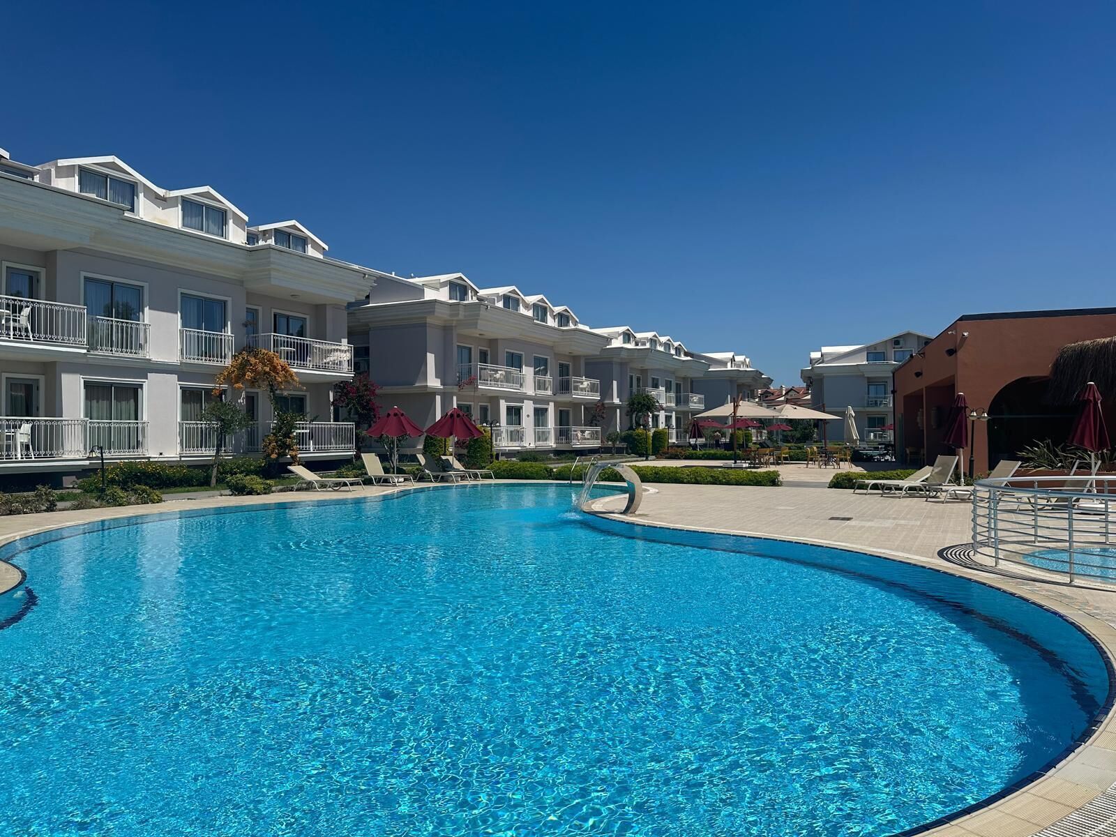 A swimming pool with lounge chairs and umbrellas, surrounded by multi-story buildings with balconies.