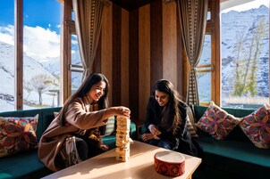 Dos personas juegan a Jenga sobre una mesa de madera en una habitación con ventanas amplias y vistas a montañas nevadas.