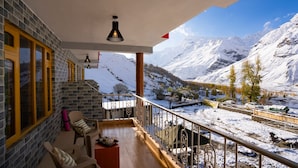 Ein Balkon mit Blick auf schneebedeckte Berge, eine Steinmauer und ein Stuhl.