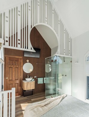 Ein modernes Badezimmer mit einem Holzwaschtisch, einem runden Spiegel, einer Duschkabine aus Glas und einer weißen Treppe mit kreisförmigen Ausschnitten.