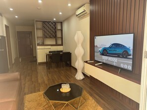 Ein modernes Wohnzimmer mit Flachbildfernseher, Holzboden, Essbereich und einer Küche mit Einbauküchenschränken.