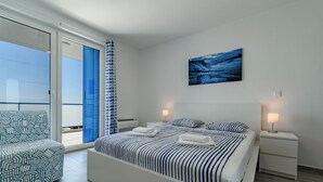 Un dormitorio moderno con una cama grande, una silla, un balcón y un cuadro en la pared.