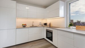 Una cocina moderna con muebles blancos, horno empotrado, microondas y un lavamanos.
