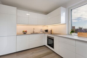 A modern kitchen with white cabinetry, a built-in oven, a microwave, and a sink. - Villa Aster (Privlaka)