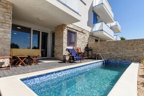 A modern pool area with a stone wall, a covered seating area, and a clear blue pool. - Villa Aster (Privlaka)