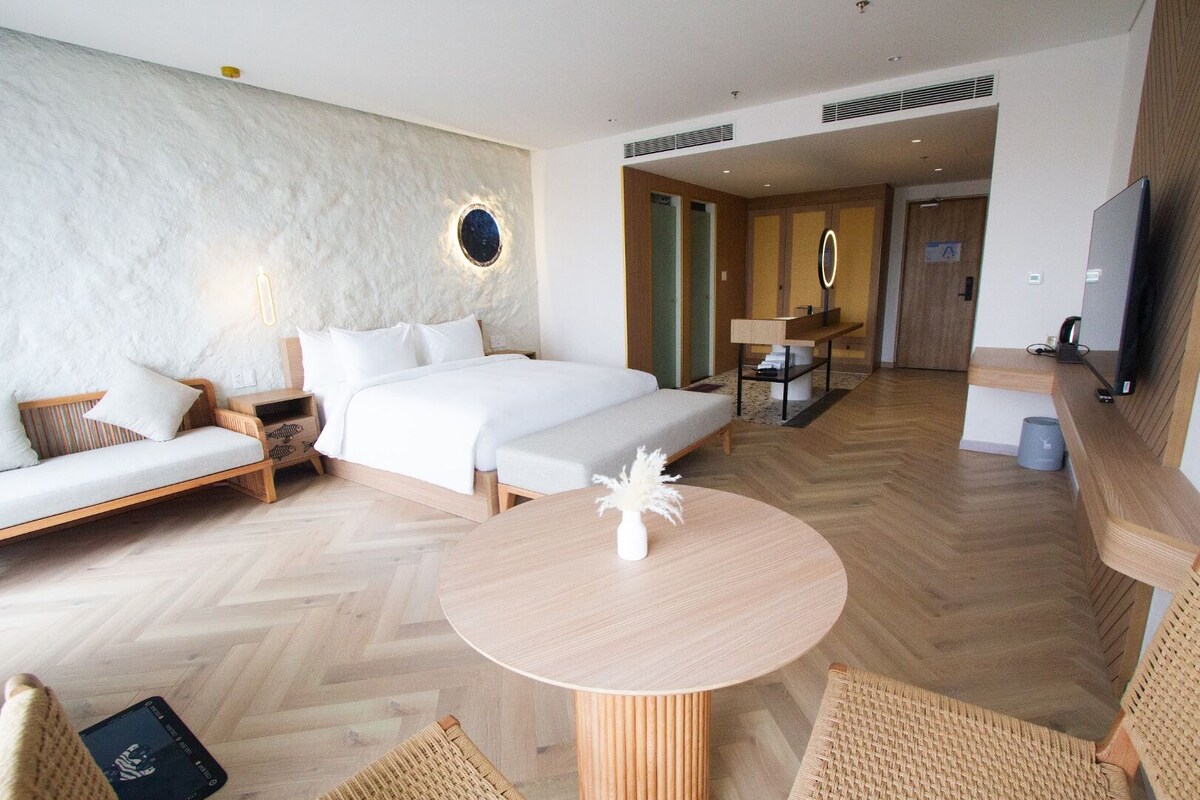 Habitación de hotel con cama, sofá, una mesa redonda, televisor y un baño visible a través de una puerta abierta.