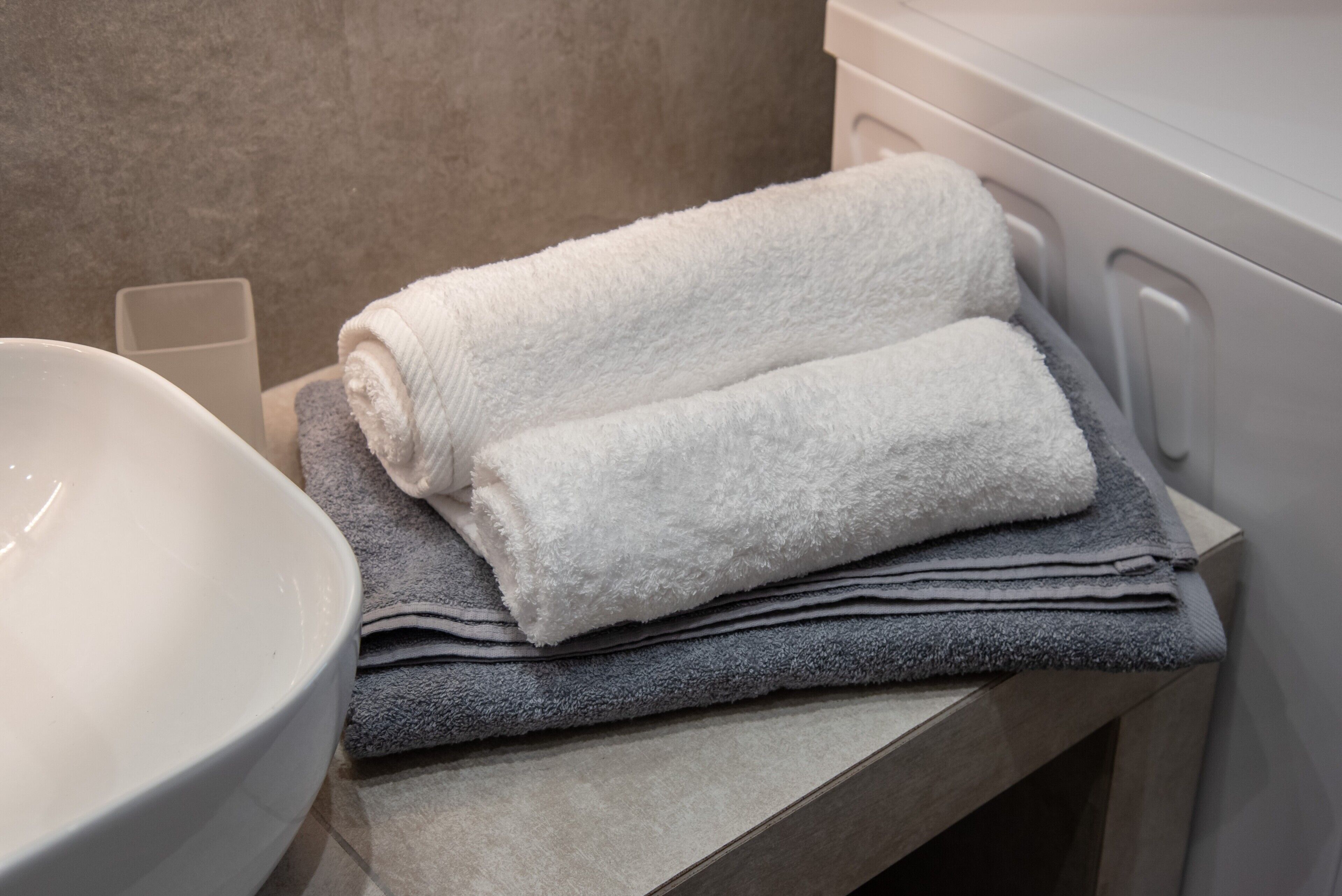 A bathroom with a white sink, a towel rack with folded towels, and a beige wall.