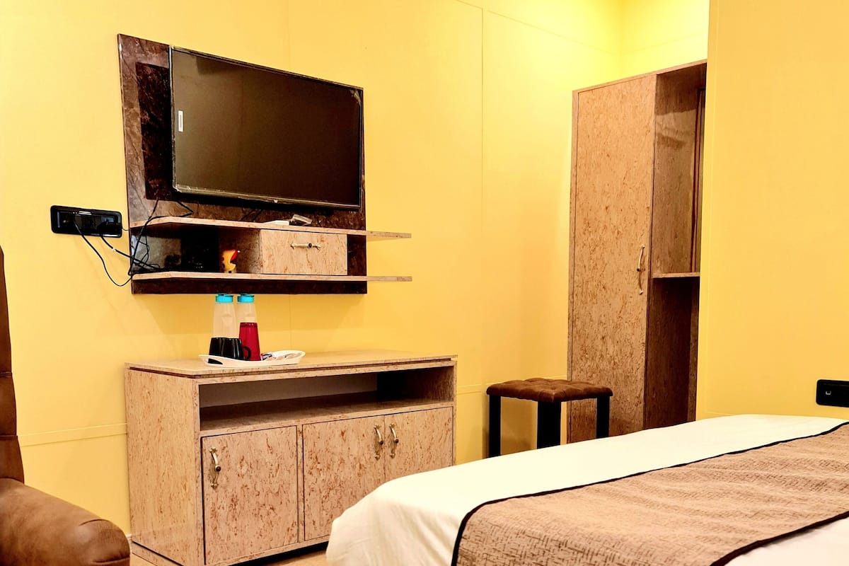 A bedroom with a bed, a TV mounted on the wall, a wooden cabinet, and a brown leather chair.