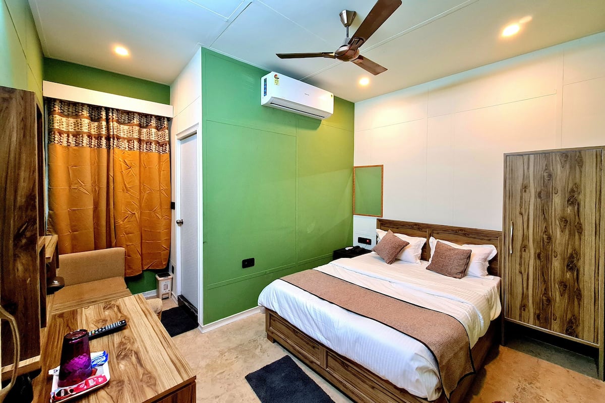 A hotel room with a bed, a desk, a chair, a ceiling fan, an air conditioning unit, and a wardrobe.