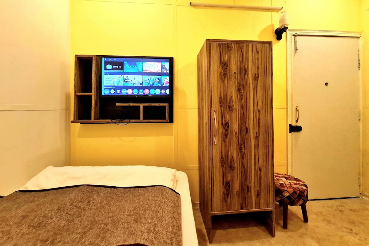 A bedroom with a bed, a TV mounted on the wall, a wardrobe, and a door.