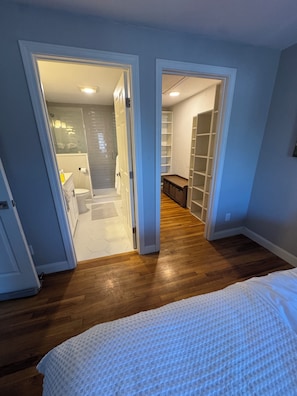 A bedroom with a bed, wooden flooring, and a hallway leading to a bathroom and closet.