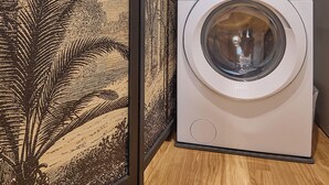 A washing machine in a room with wooden flooring and a large, patterned tapestry on the wall. - BRIGHT LUXURY APARTMENT (Milano)