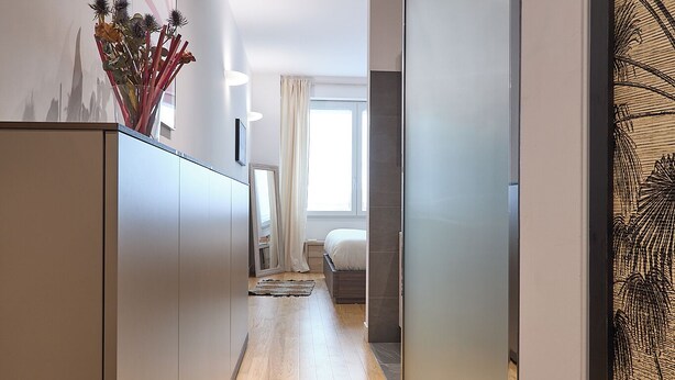 A modern hallway with a wooden floor, a bed with a white headboard, and a large mirror on the wall. - BRIGHT LUXURY APARTMENT (Milano)