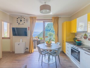 A modern kitchen with a dining area, a TV, and a view of a mountainous landscape. - EnjoyIseoLake - Blooming Lakefront (Lombardia)