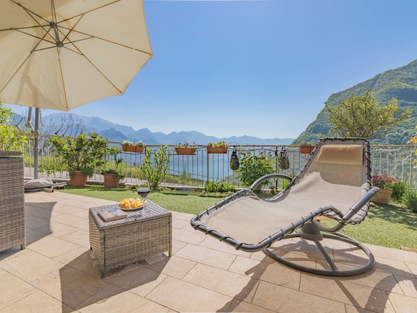 A patio with a wicker table, a cushioned chair, and an umbrella.