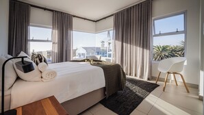 A modern hotel room with a large bed, a bedside table, a chair, and a view of the city.