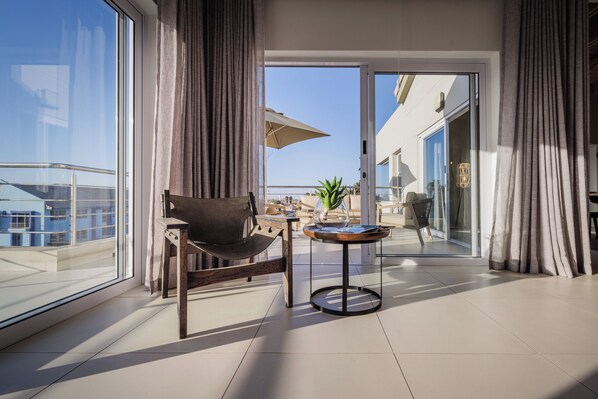 Ein modernes Zimmer mit einem großen Fenster, einem Sessel, einem kleinen runden Tisch und Blick ins Freie.