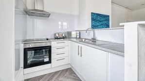 Eine moderne Küche mit weißen Schränken, einem eingebauten Ofen, einer Mikrowelle, einem Toaster und einer Spüle aus Edelstahl.