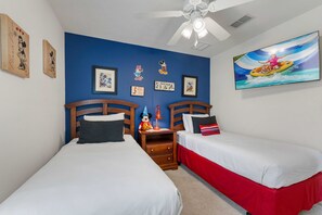 Ein Zimmer mit zwei Betten, einem Deckenventilator, Wandbildern und einem Fernseher.