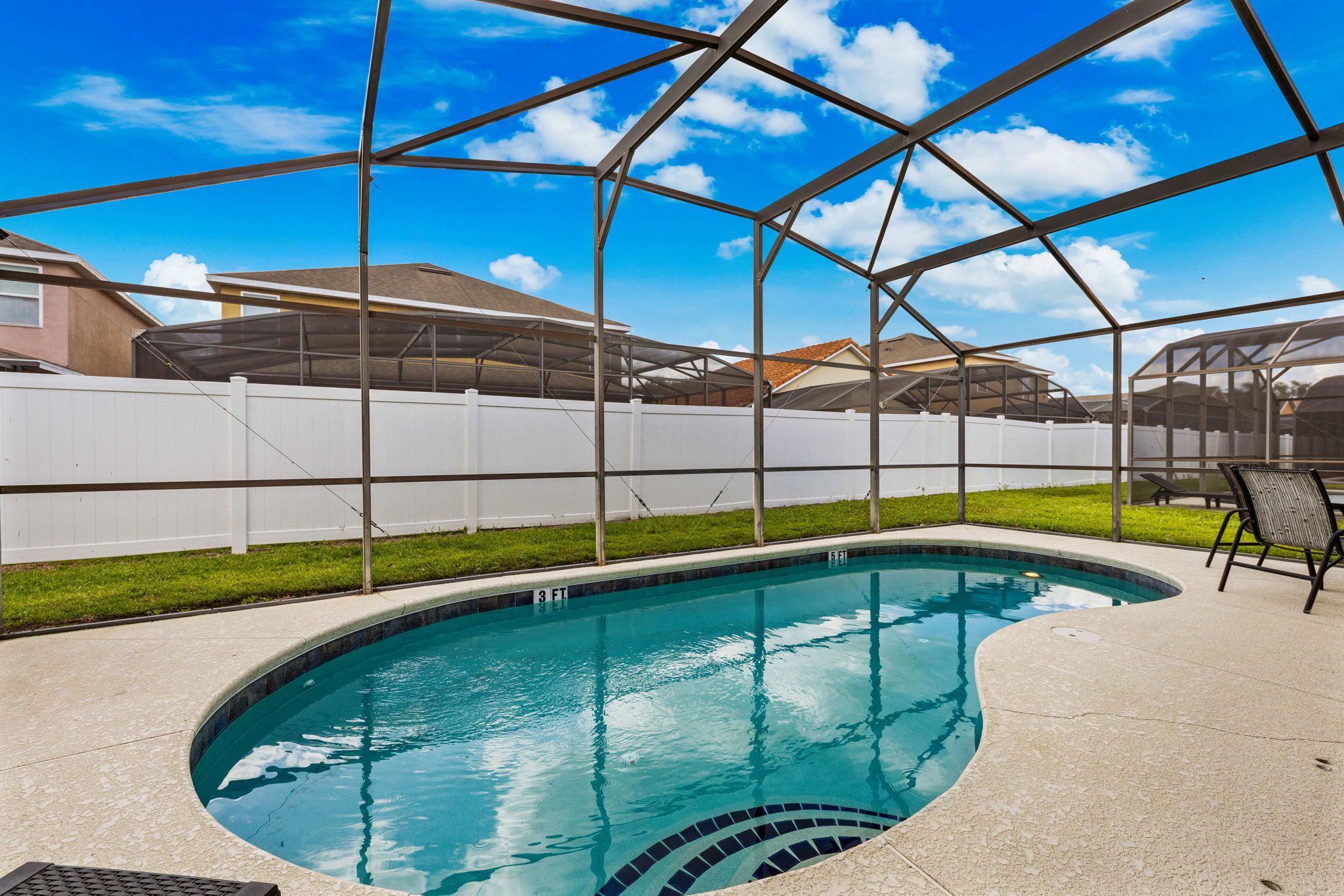 A swimming pool with a white fence, a covered patio area, and a clear blue sky.