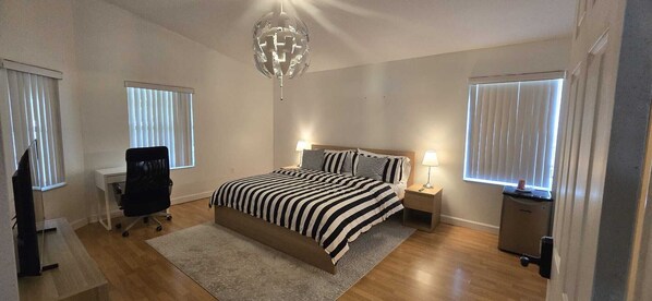 A bedroom with a bed, bedside tables, a desk, a chair, and a hanging light fixture.