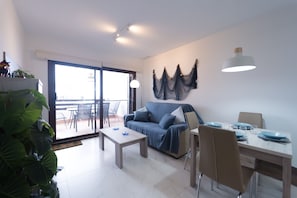 Moderni olohuone, jossa on sohva, sohvapöytä, ruokapöytä ja tuolit. Huoneesta on pääsy parvekkeelle, josta on näkymä. Seinällä on koriste-elementti ja huoneessa on myös riippuvalaisin.