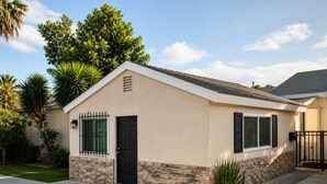A single-story house with a beige exterior, a black door, and a window with shutters. - Private studio in north Long Beach with refreshing AC (Long Beach)